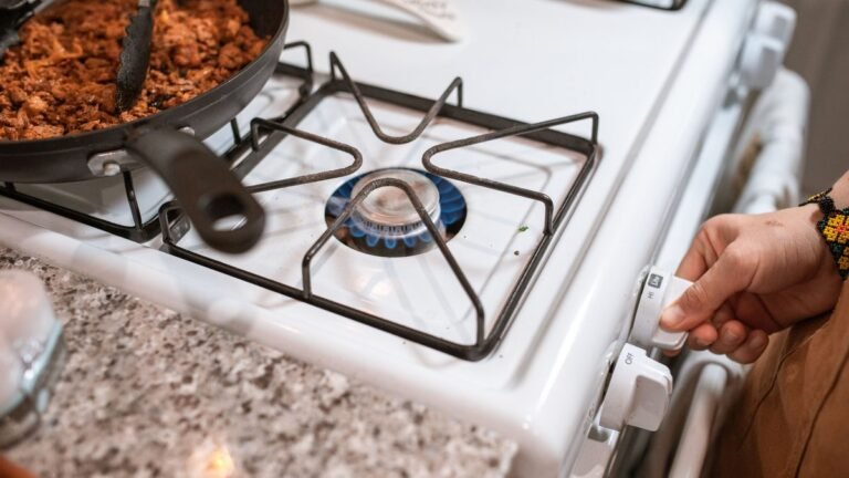 Mão acendendo a boca do fogão a gás em uma cozinha simples