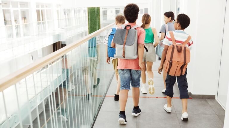 Estudantes de mochila caminhando no corredor da escola, vistos de costas