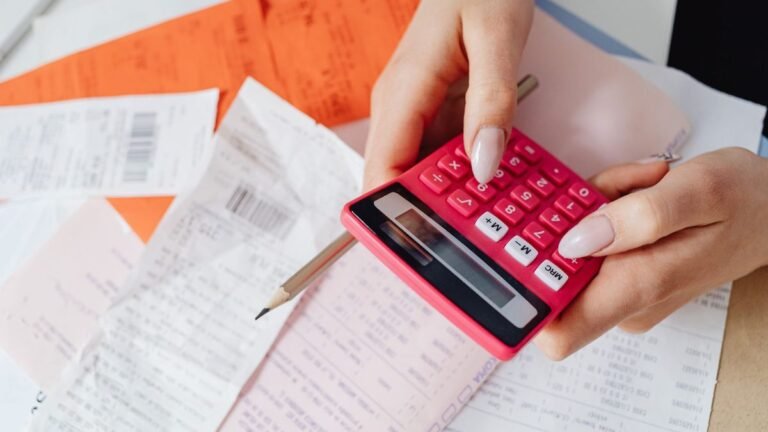 Mão fazendo contas numa calculadora rosa sobre boletos e recibos
